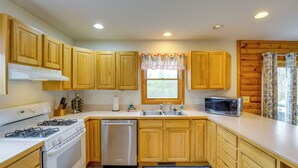 A kitchen with wooden cabinets, a stove, a dishwasher, a microwave, and a window with a floral valance. - Fire Pit & Grill! Spacious Port Huron Home By Dtwn (Port Huron)