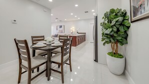 Een moderne keuken met witte kasten, een eettafel met stoelen en een grote potplant.