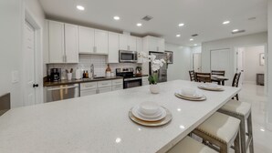 Een moderne keuken met witte kasten, een centraal eiland met een bloevas, en een eetgedeelte met een tafel voor vier personen.