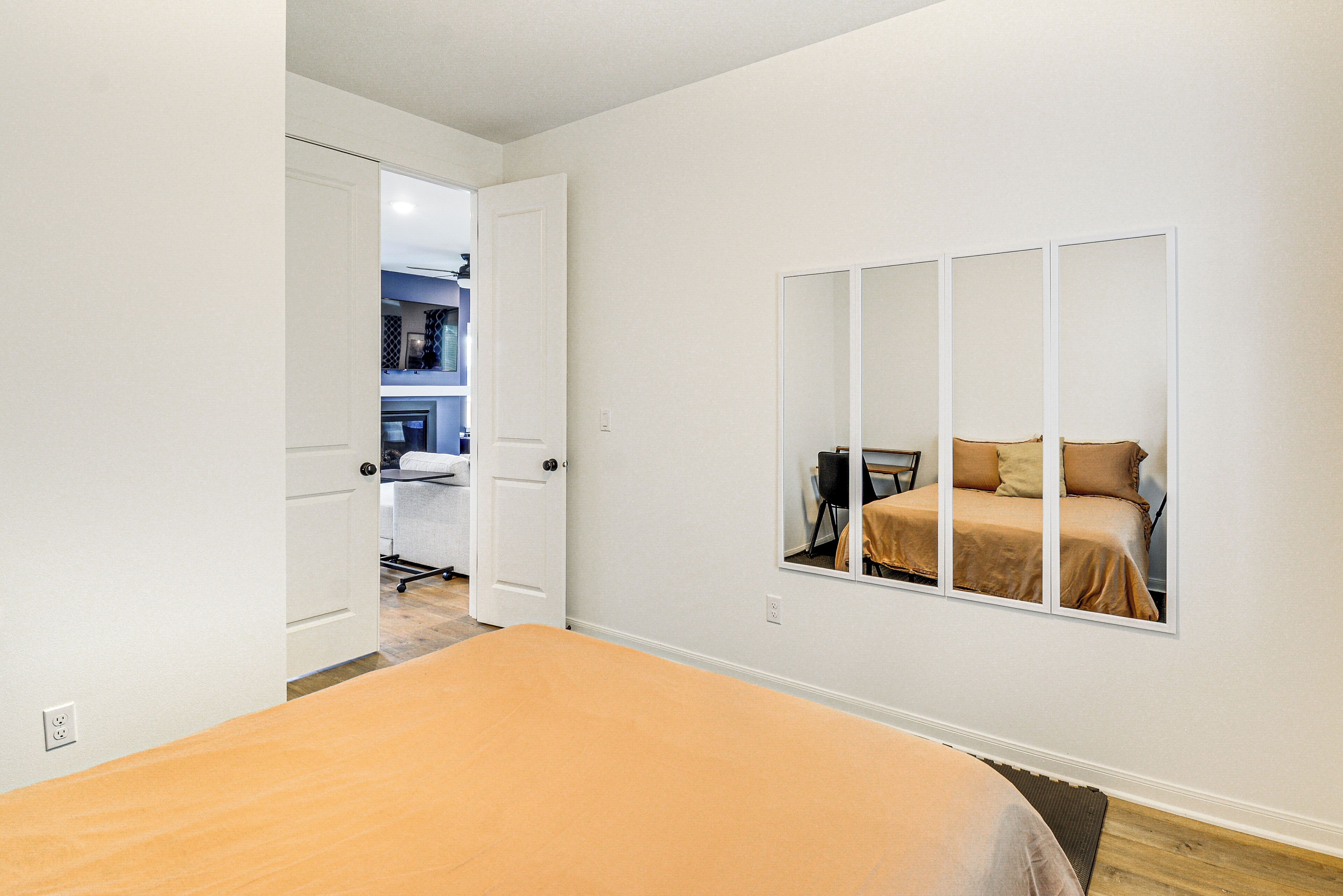 A bedroom with a bed, a large mirror, and a door leading to a kitchenette.
