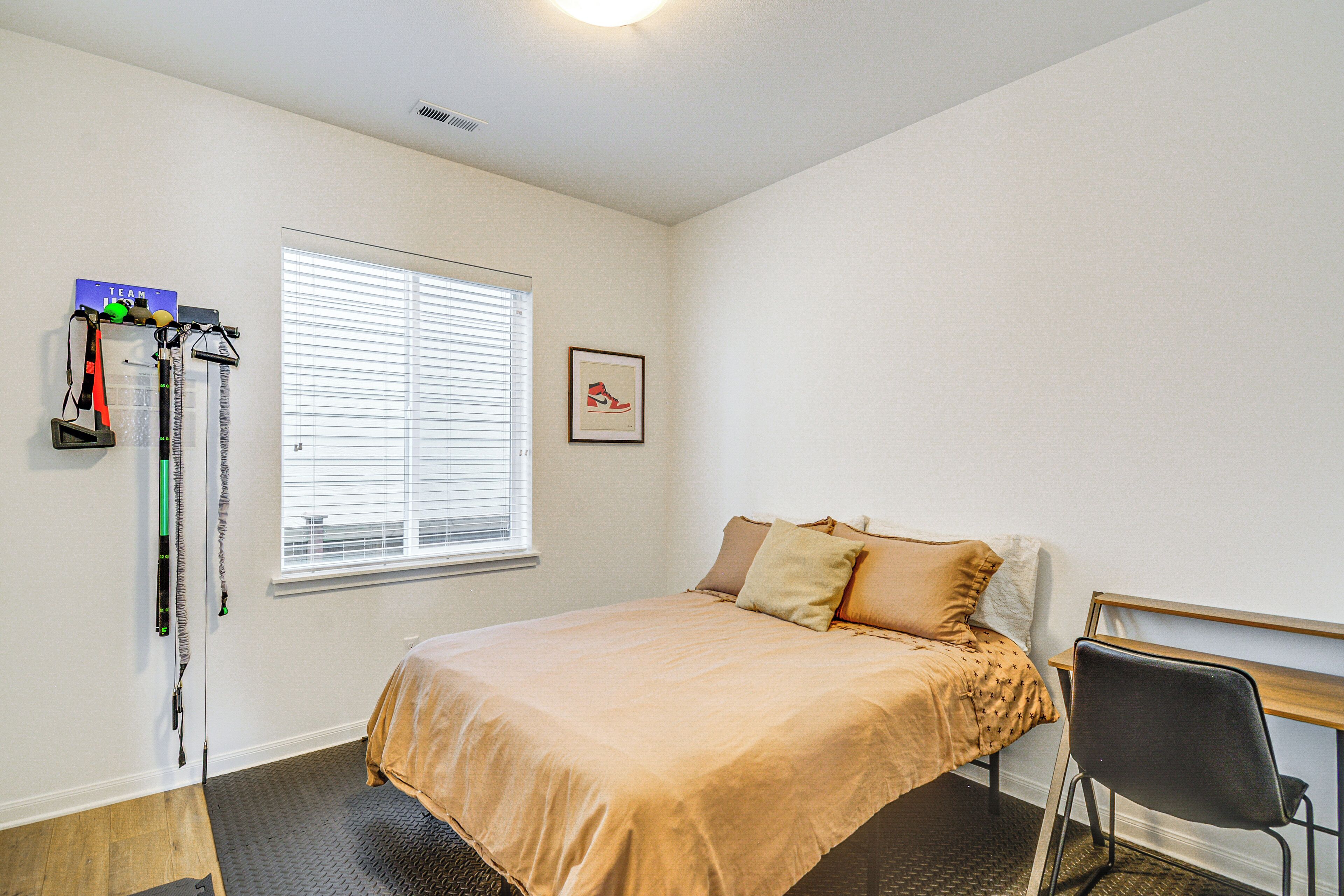 A bedroom with a bed, a window with blinds, a chair, and a wall-mounted rack with items.