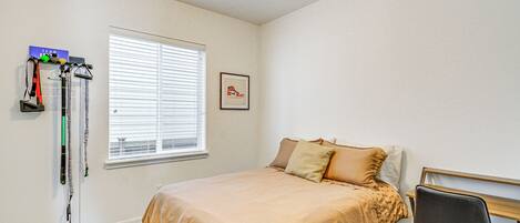 A bedroom with a bed, a window with blinds, a chair, and a wall-mounted rack with items.