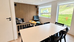 A modern interior with a dining table, chairs, a sofa, and a view of a green landscape through large windows. - Hvanngarðs Smáttan við Stórá (Dalur)