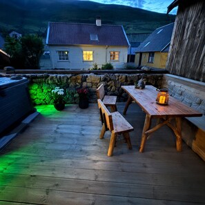 Une terrasse en bois avec une table et des bancs, un jacuzzi et un mur en pierre.