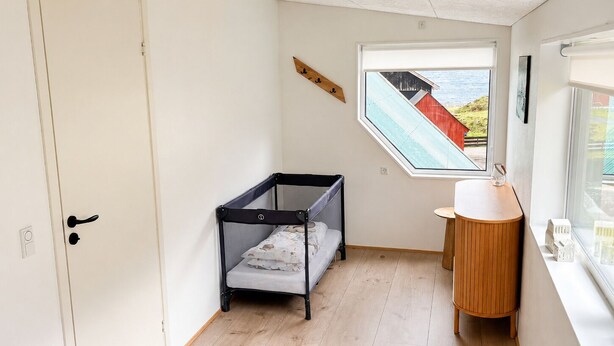 A room with a bunk bed, a small wooden table, a window with a view of a red building, and a white door. - Hvanngarðs Smáttan við Stórá (Dalur)