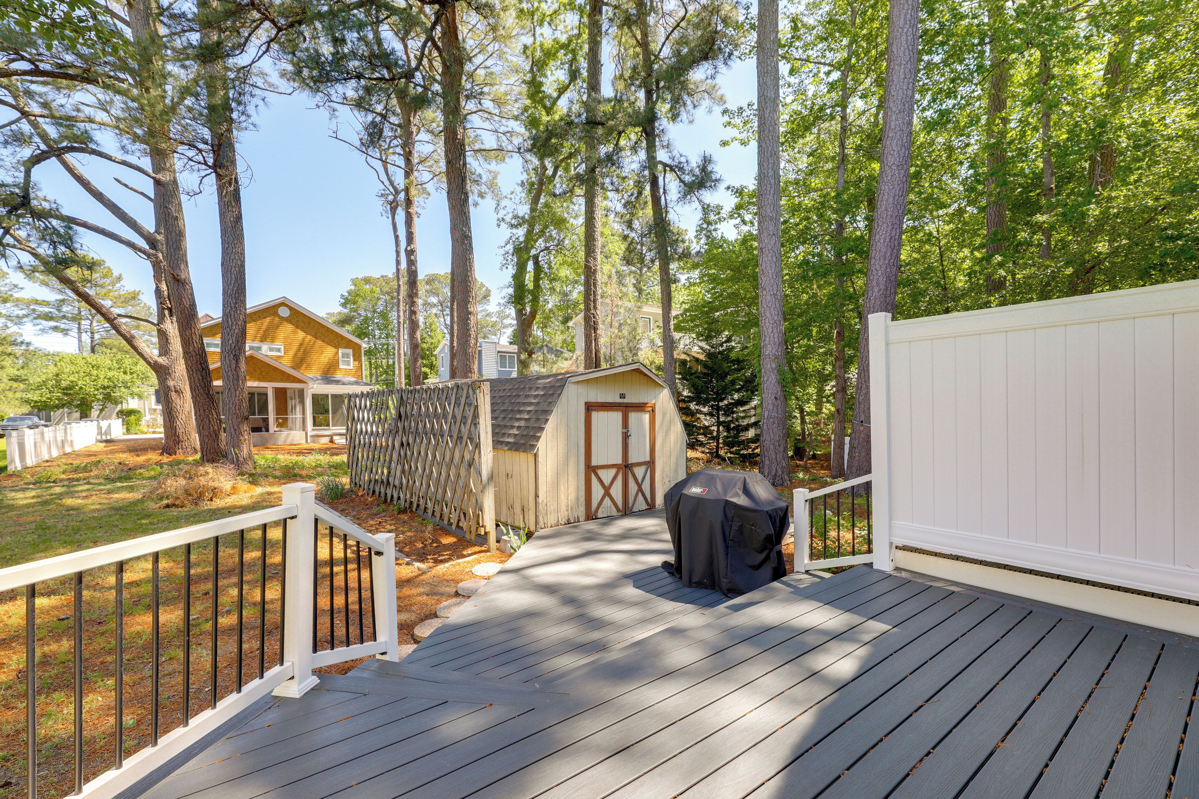 Une terrasse en bois avec une rambarde blanche, un petit abri de jardin et un espace barbecue couvert.