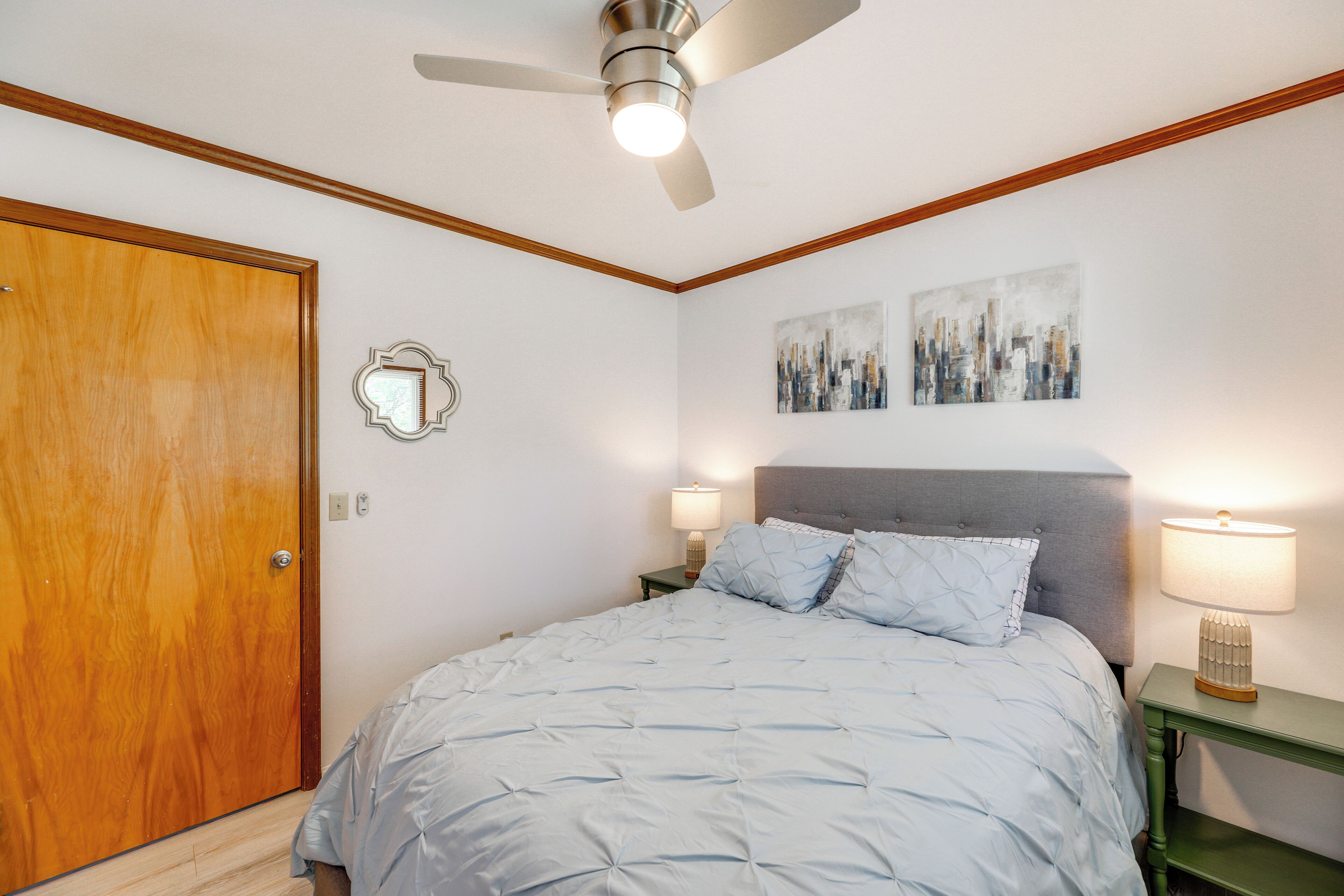 Une chambre à coucher avec un lit, un ventilateur de plafond, une table de chevet avec une lampe et une porte.