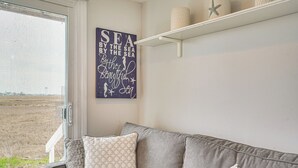 A room with a grey sofa, a wall with a sea-themed artwork, and a view of the outdoors. - Coastal Hampton Condo: Walk to North Beach! (Hampton)