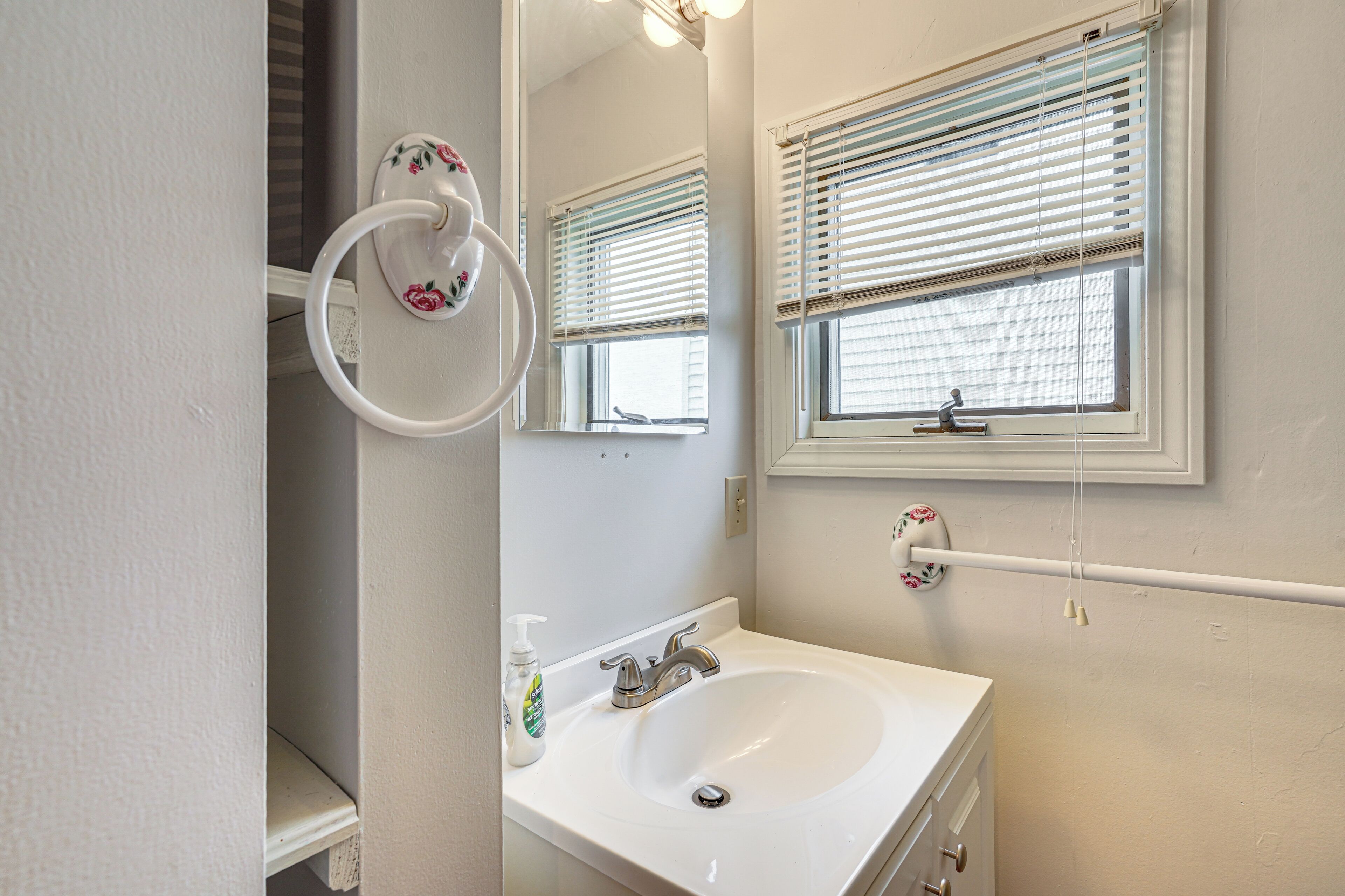 A bathroom with a white sink, a mirror, and a window with blinds.
