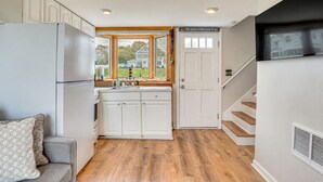 A kitchen with white cabinets, a refrigerator, a window with a view of houses, and a door with a sign. - Coastal Hampton Condo: Walk to North Beach! (Hampton)
