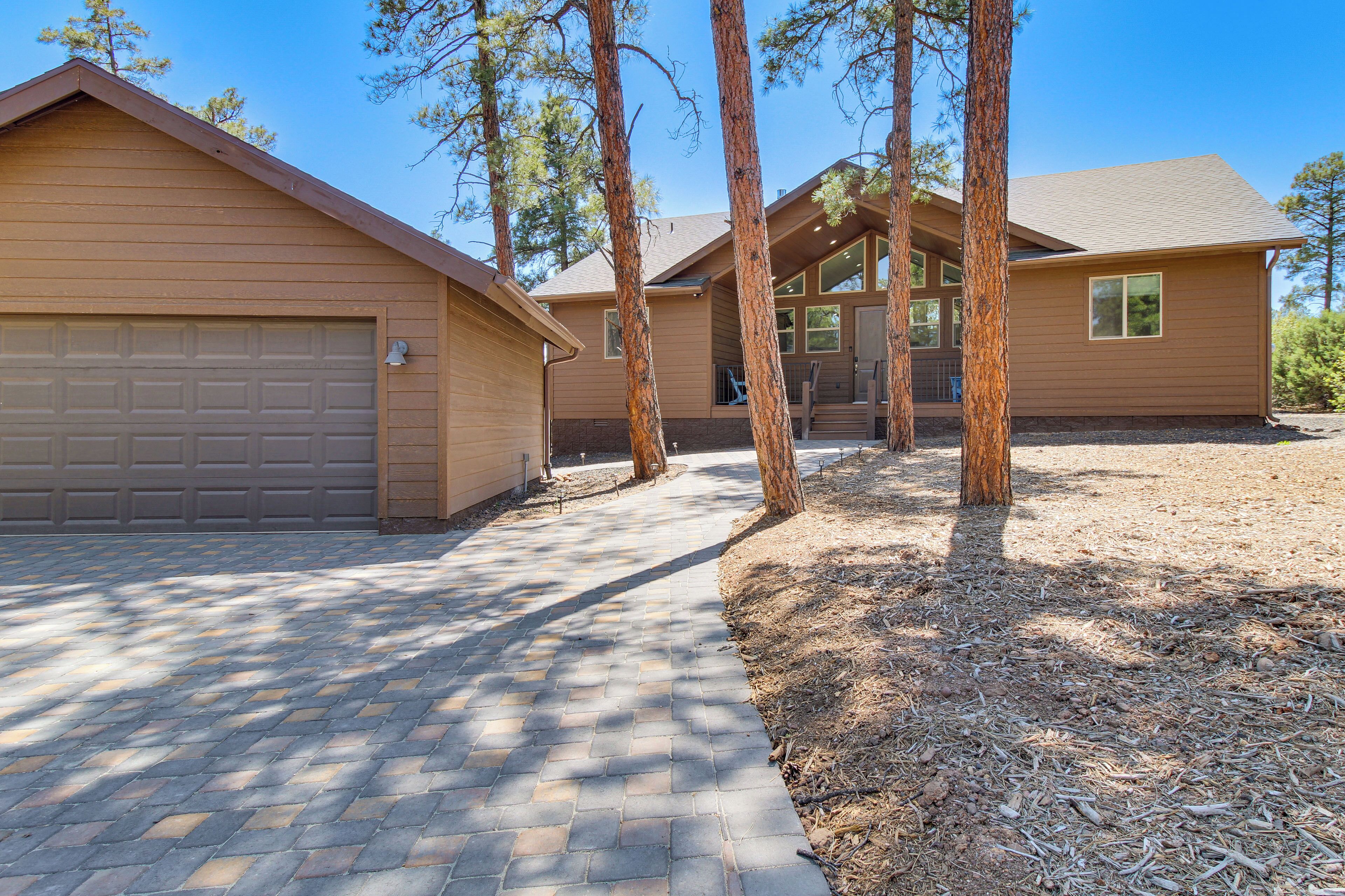 A two-story house with a garage, a paved driveway, and a wooded area with tall trees.