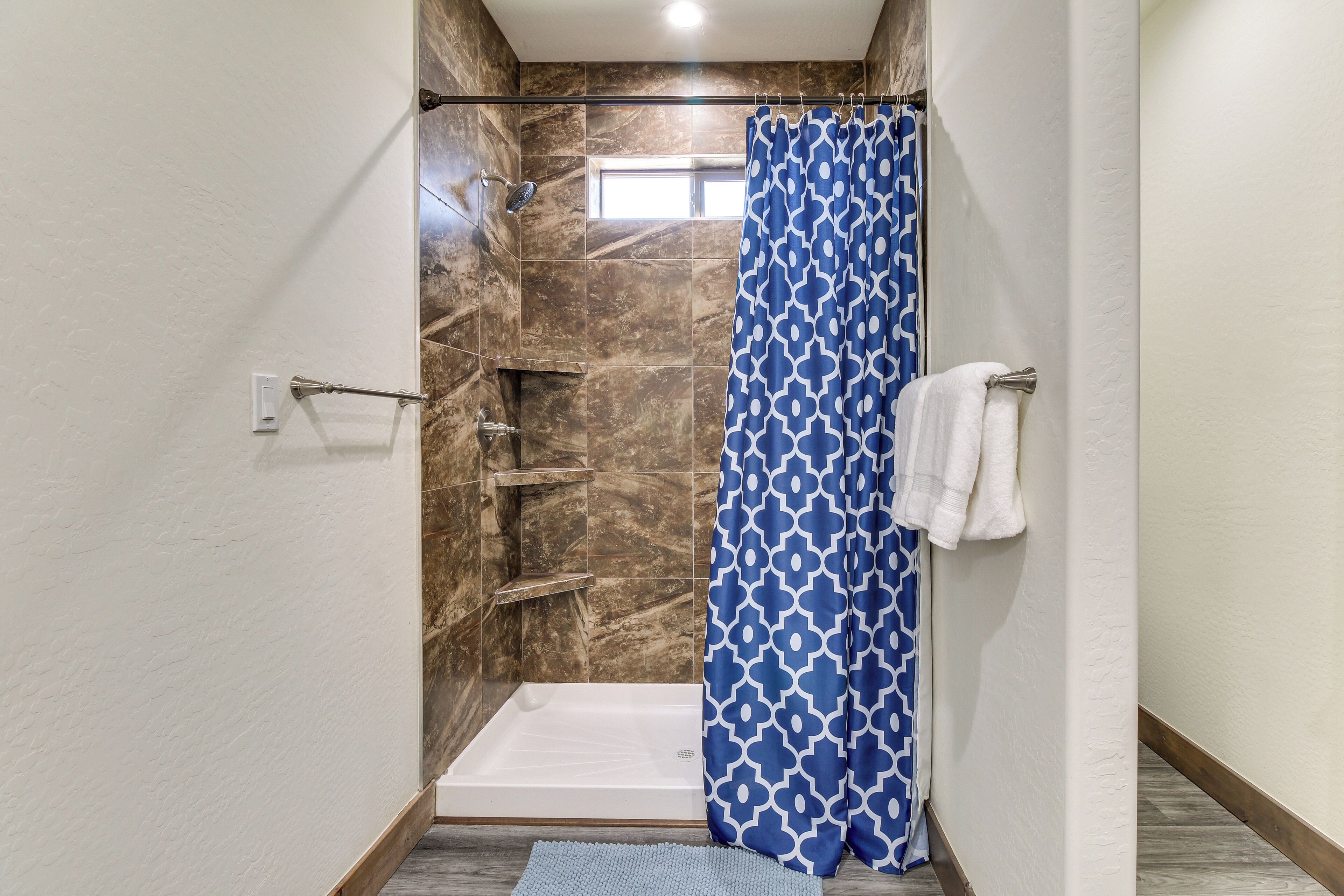 A shower area with a patterned curtain, a towel rack, and a small window.