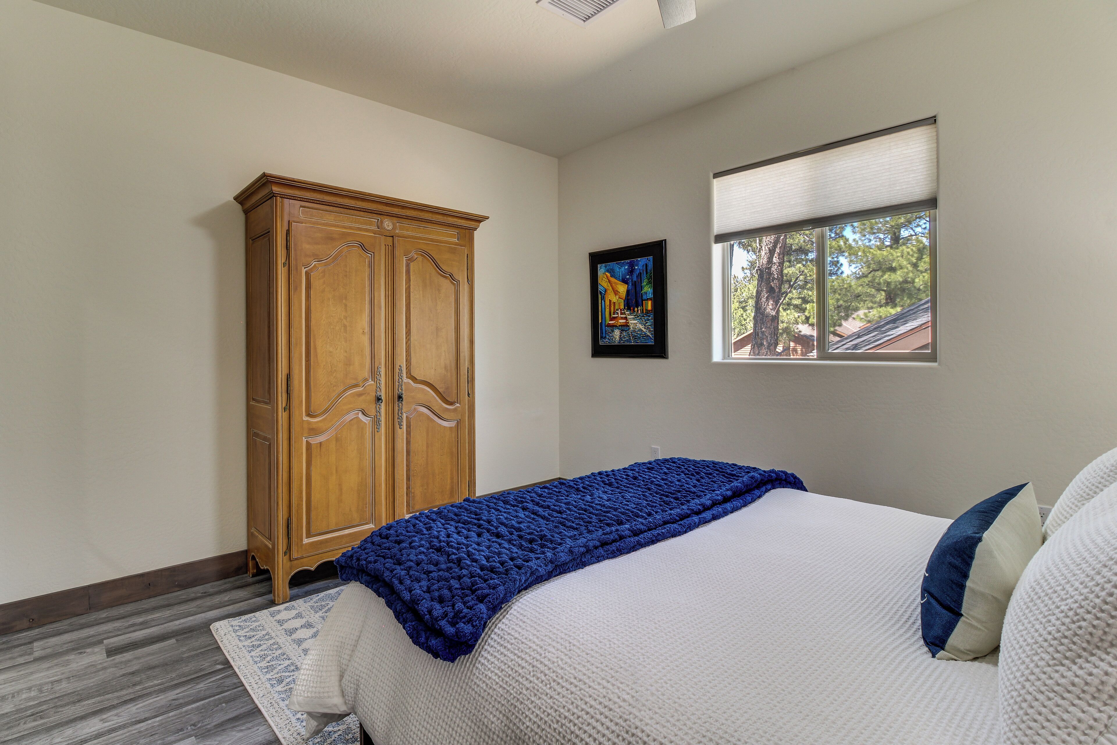 Ein Schlafzimmer mit einem Bett, einem Holzschrank, einem Fenster mit Jalousien und einem gerahmten Bild an der Wand.