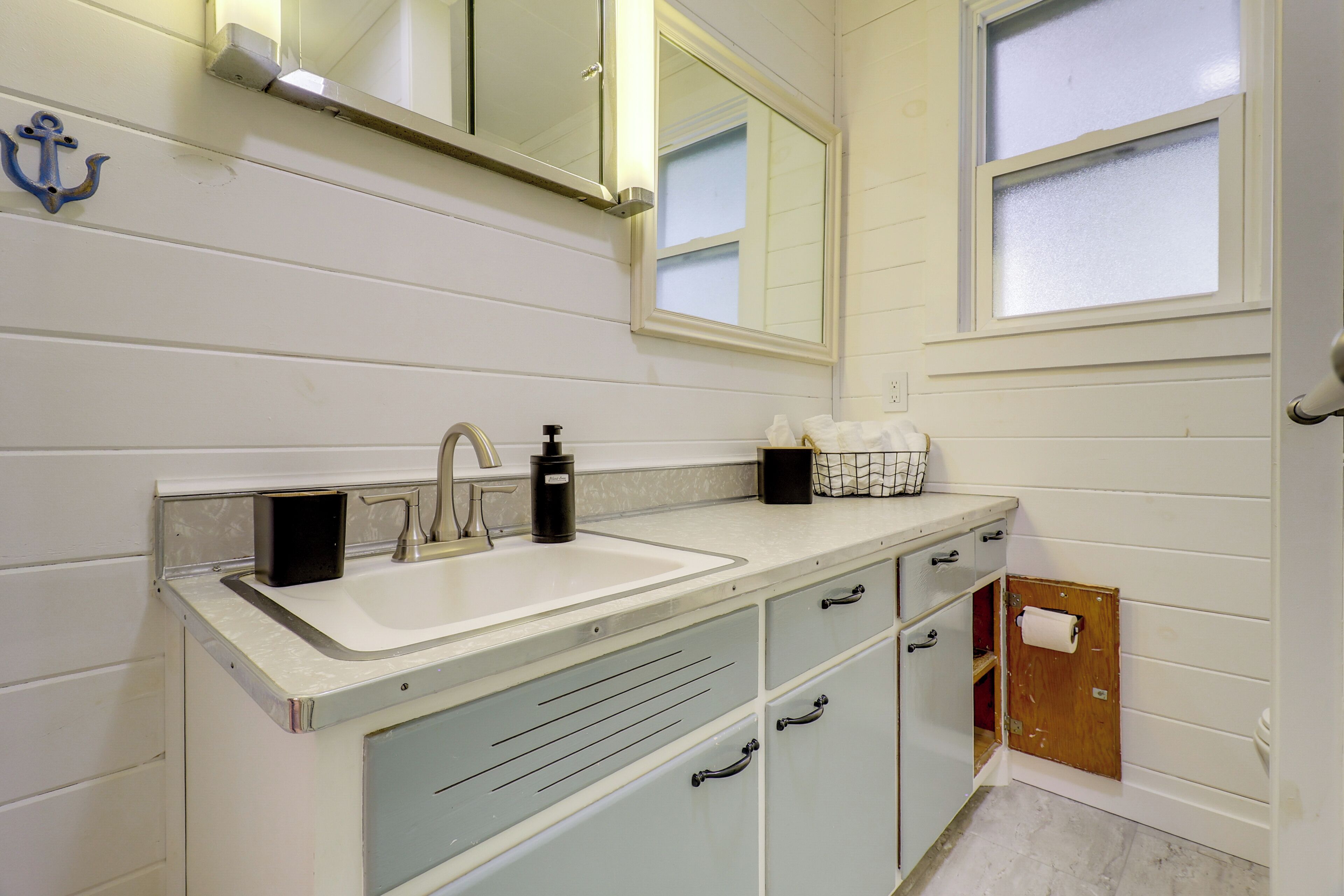 Une salle de bain avec un lavabo blanc, un miroir et une fenêtre.