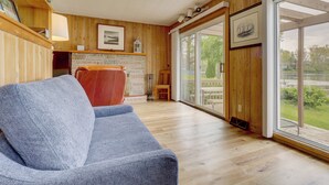 A wooden interior with a blue sofa, a fireplace, and large windows. - Lake Webster Retreat: Pier, Kayaks & Fire Pit (North Webster)