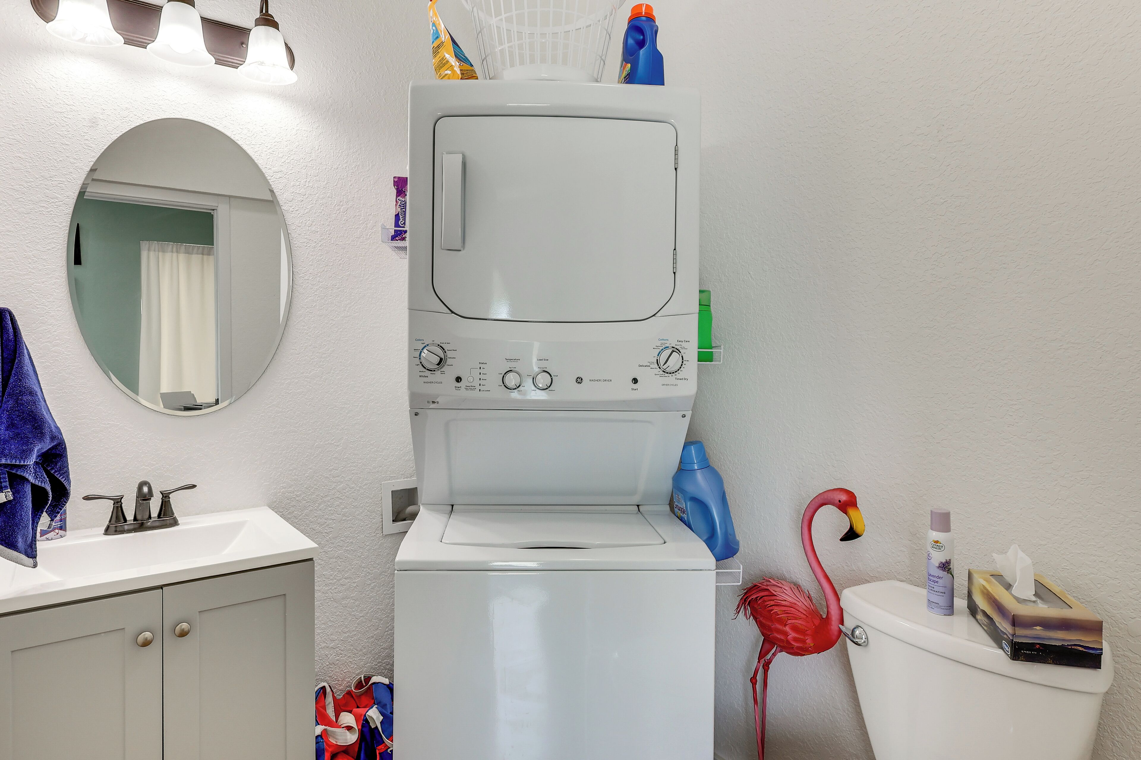 A compact bathroom with a washing machine, a toilet, a sink, and a mirror.