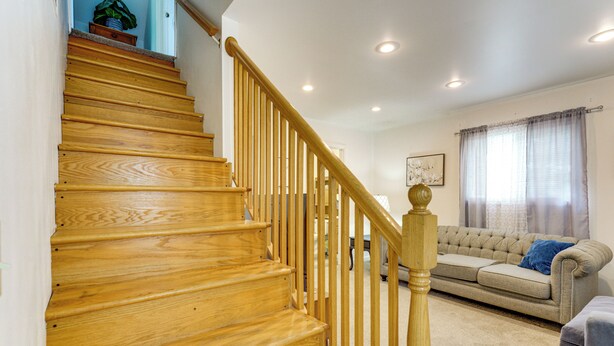 Un escalier en bois avec une rampe, un canapé beige et une fenêtre avec des rideaux.