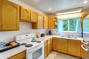 Una cocina con armarios de madera, una estufa blanca, un lavamanos y una ventana con cortinas.