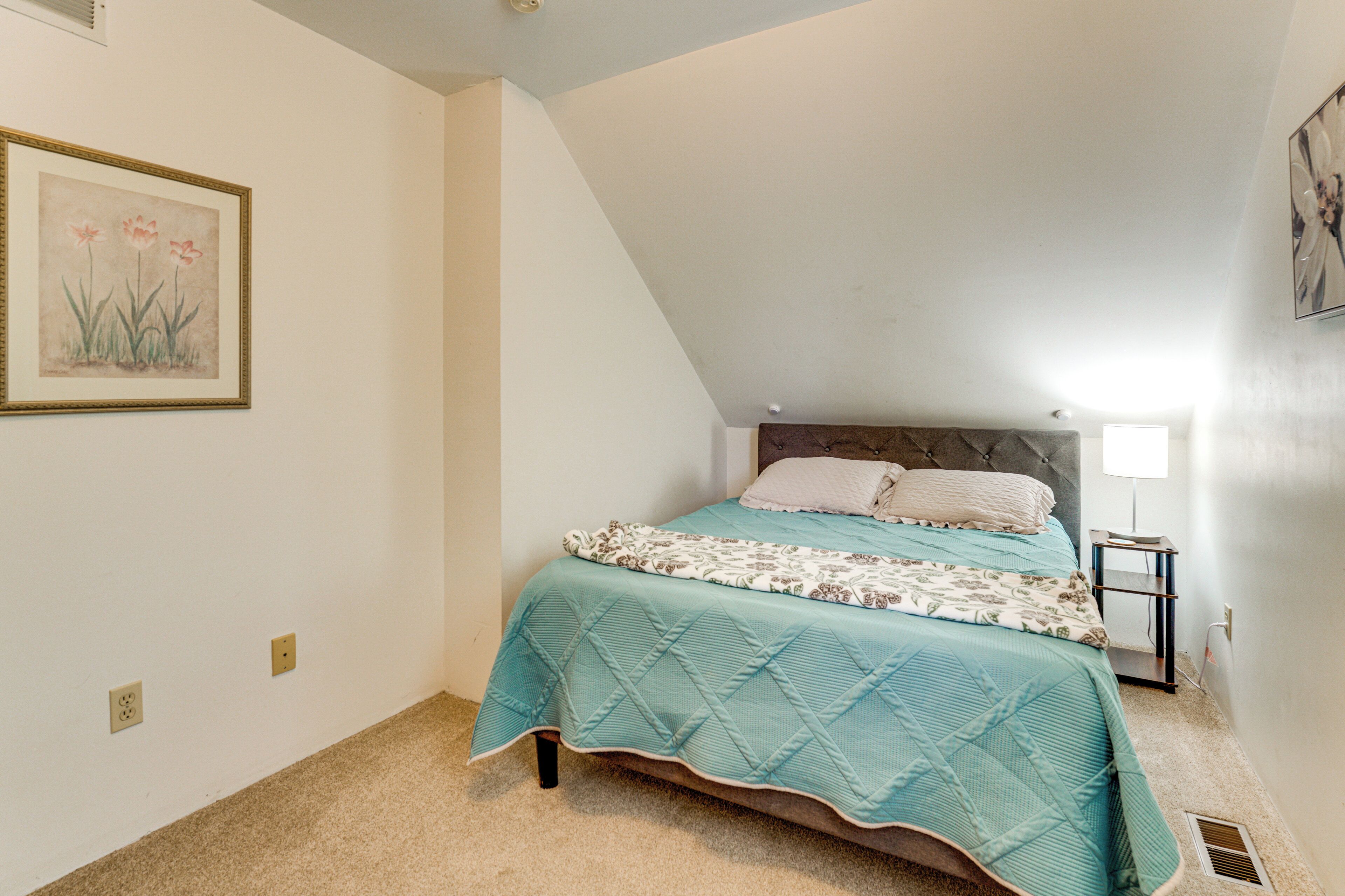 A bedroom with a bed, a nightstand, a wall-mounted lamp, and a framed picture.