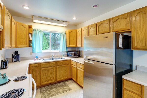 A kitchen with wooden cabinets, a stainless steel refrigerator, a microwave, and a sink.