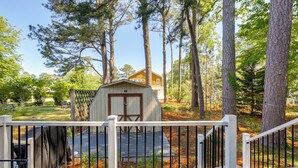 Un abri en bois avec une porte et des fenêtres, entouré d’arbres et d’une clôture blanche.