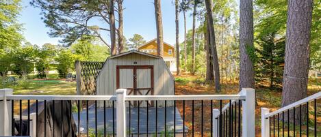 A wooden shed with a door and windows, surrounded by trees and a white fence.