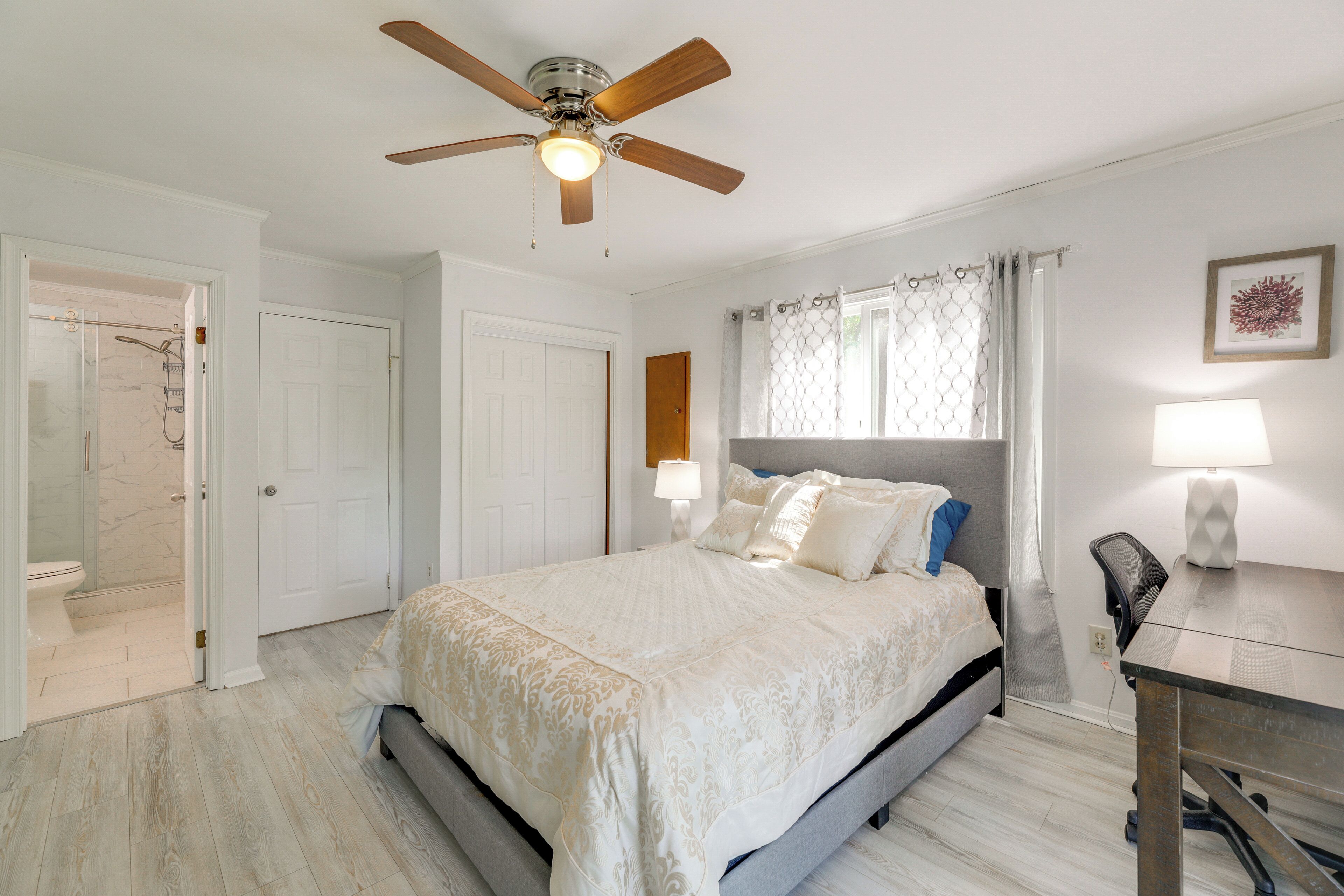 A bedroom with a bed, a desk, a chair, a ceiling fan, and a shower.