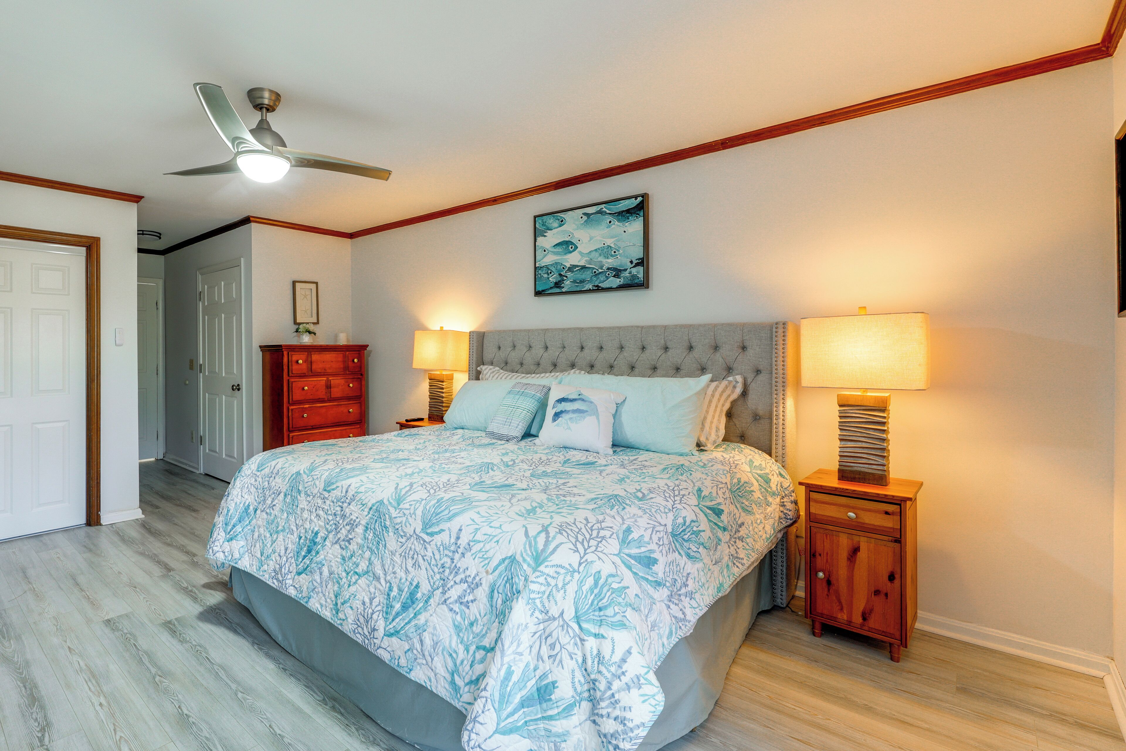 A bedroom with a bed, two bedside tables, a ceiling fan, and a wall-mounted painting.