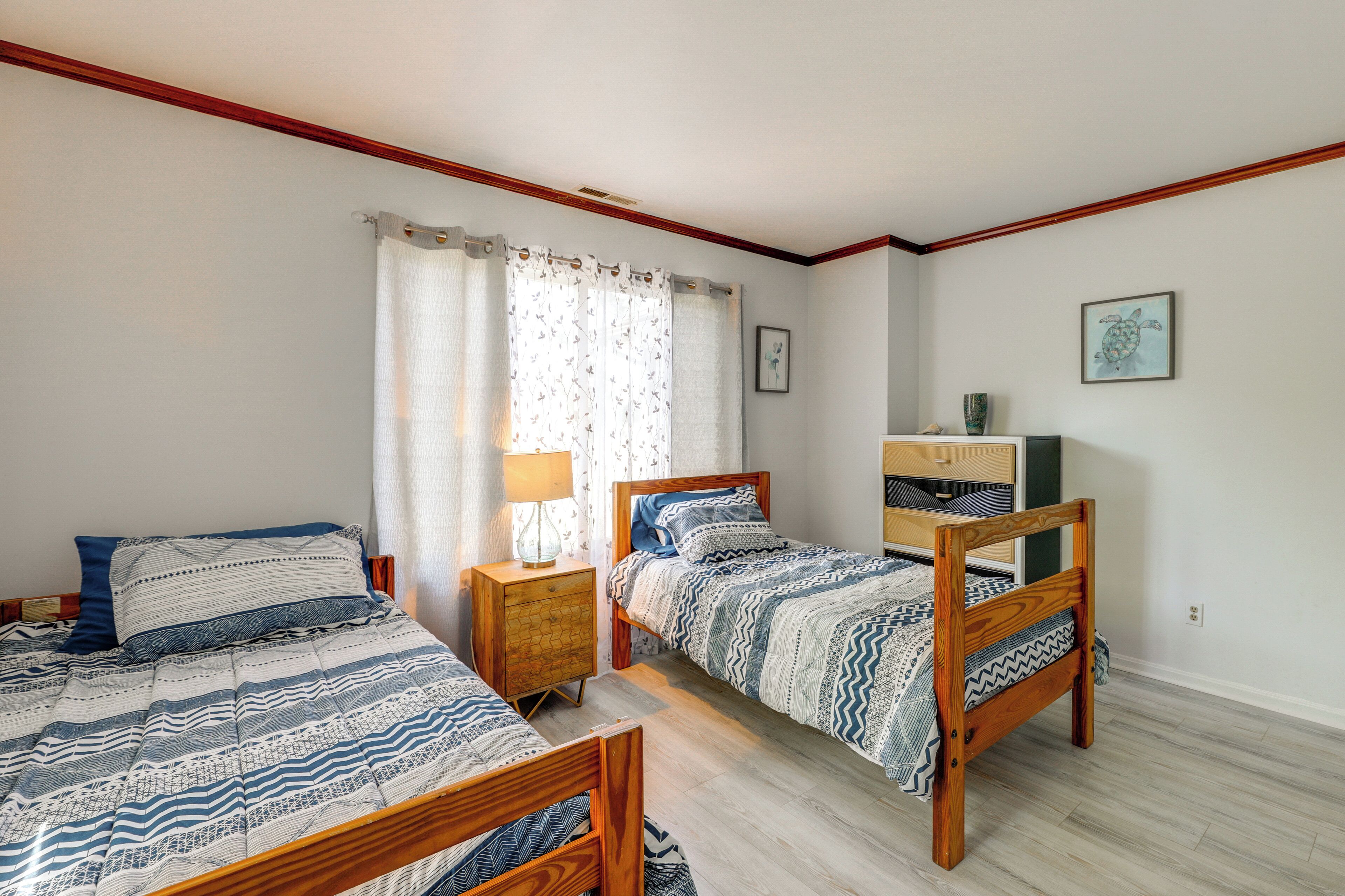 A bedroom with two wooden beds, a nightstand with a lamp, a dresser, and a framed picture on the wall.