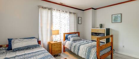 A bedroom with two wooden beds, a nightstand with a lamp, a dresser, and a framed picture on the wall.