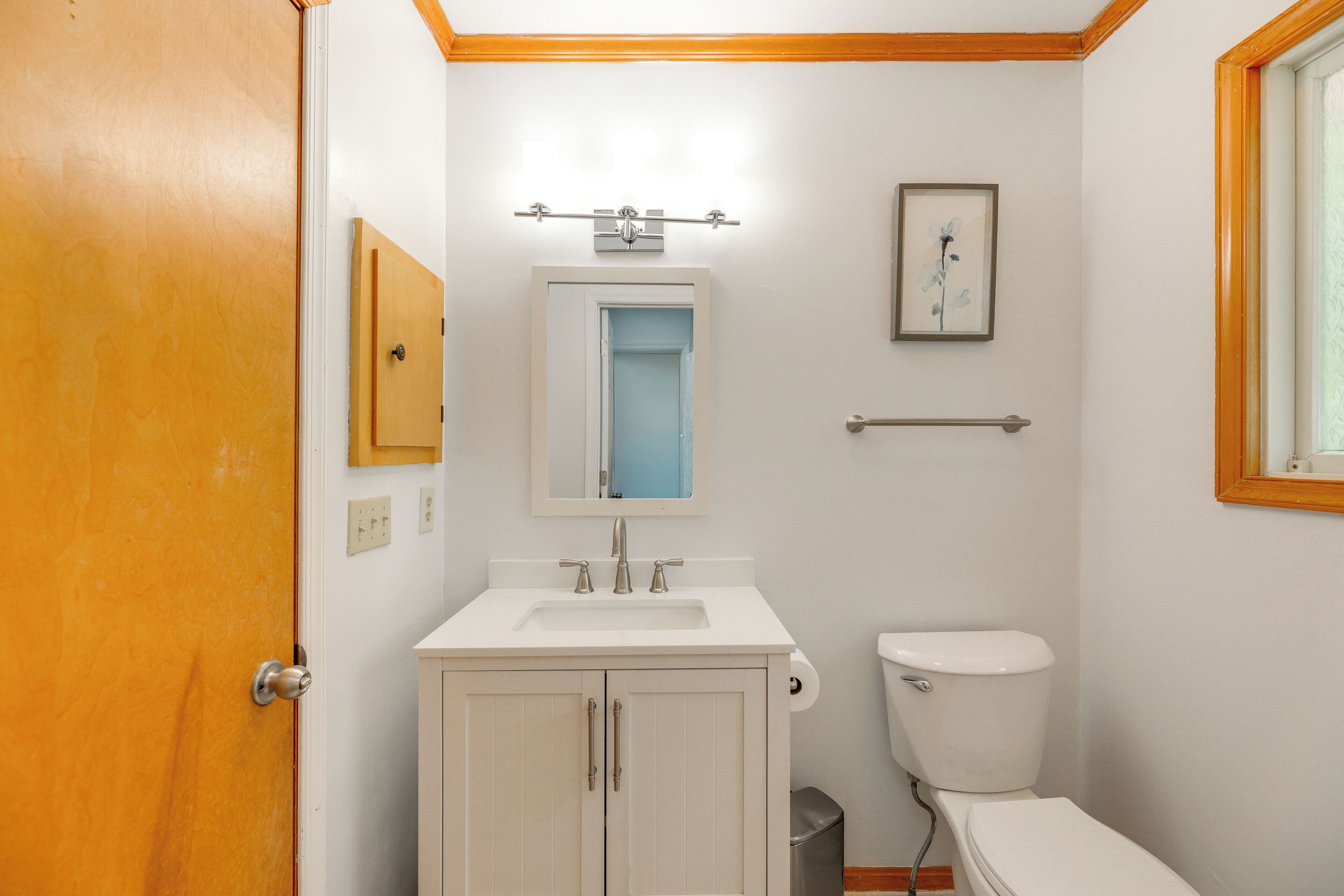 Een badkamer met een witte wasbak, een toilet, een spiegel en een ingelijst foto aan de muur.