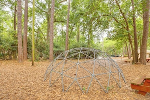 Una estructura en forma de cúpula geodésica de metal en un área boscosa con árboles y una mesa de picnic.