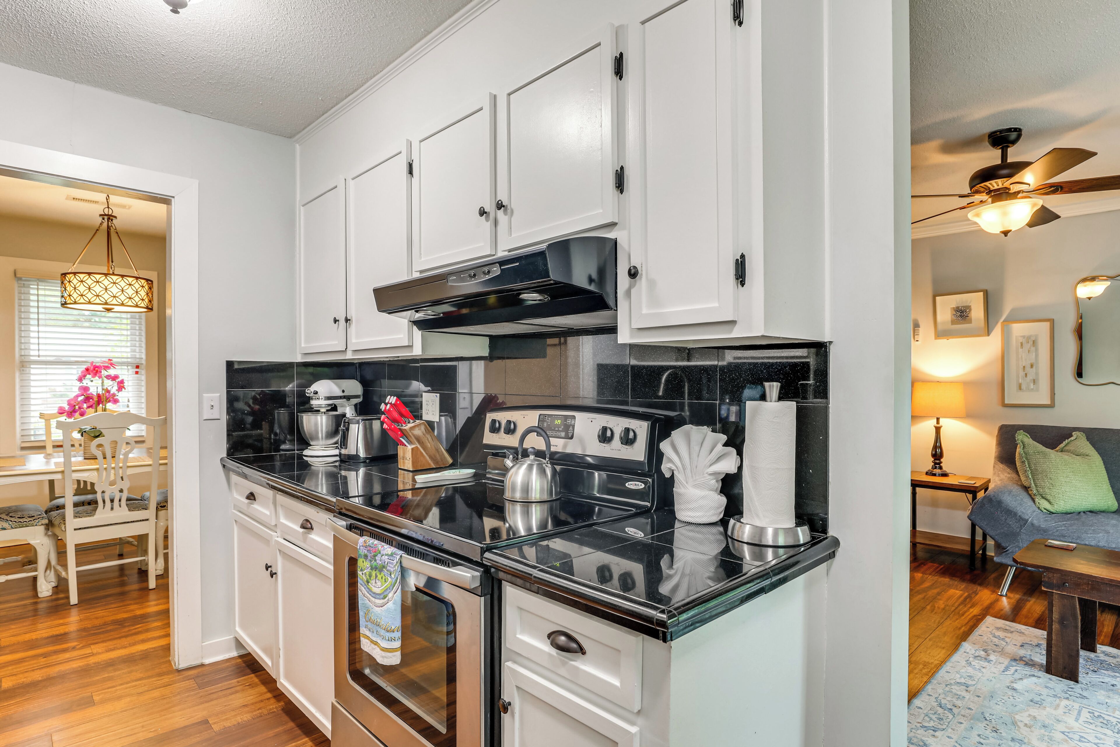 A modern kitchen with white cabinets, a black countertop, stainless steel appliances, and a dining area with a wooden table and chairs.