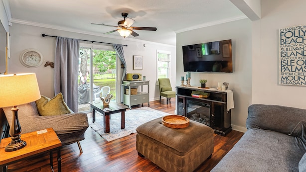 A living room with a sofa, ottoman, coffee table, TV, fireplace, and a ceiling fan.