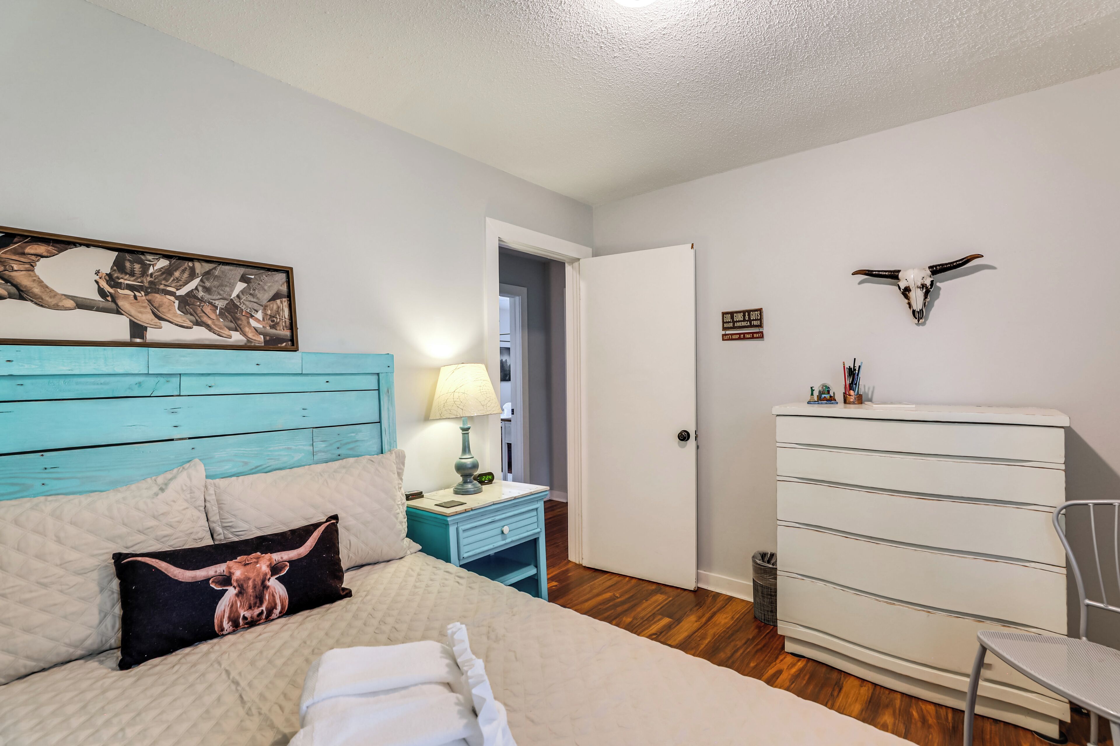 Une chambre à coucher comprenant un lit, une table de chevet, une commode et une porte donnant sur une autre pièce.