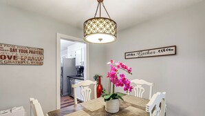 A dining area with a wooden table, white chairs, a hanging light fixture, and a wall sign.