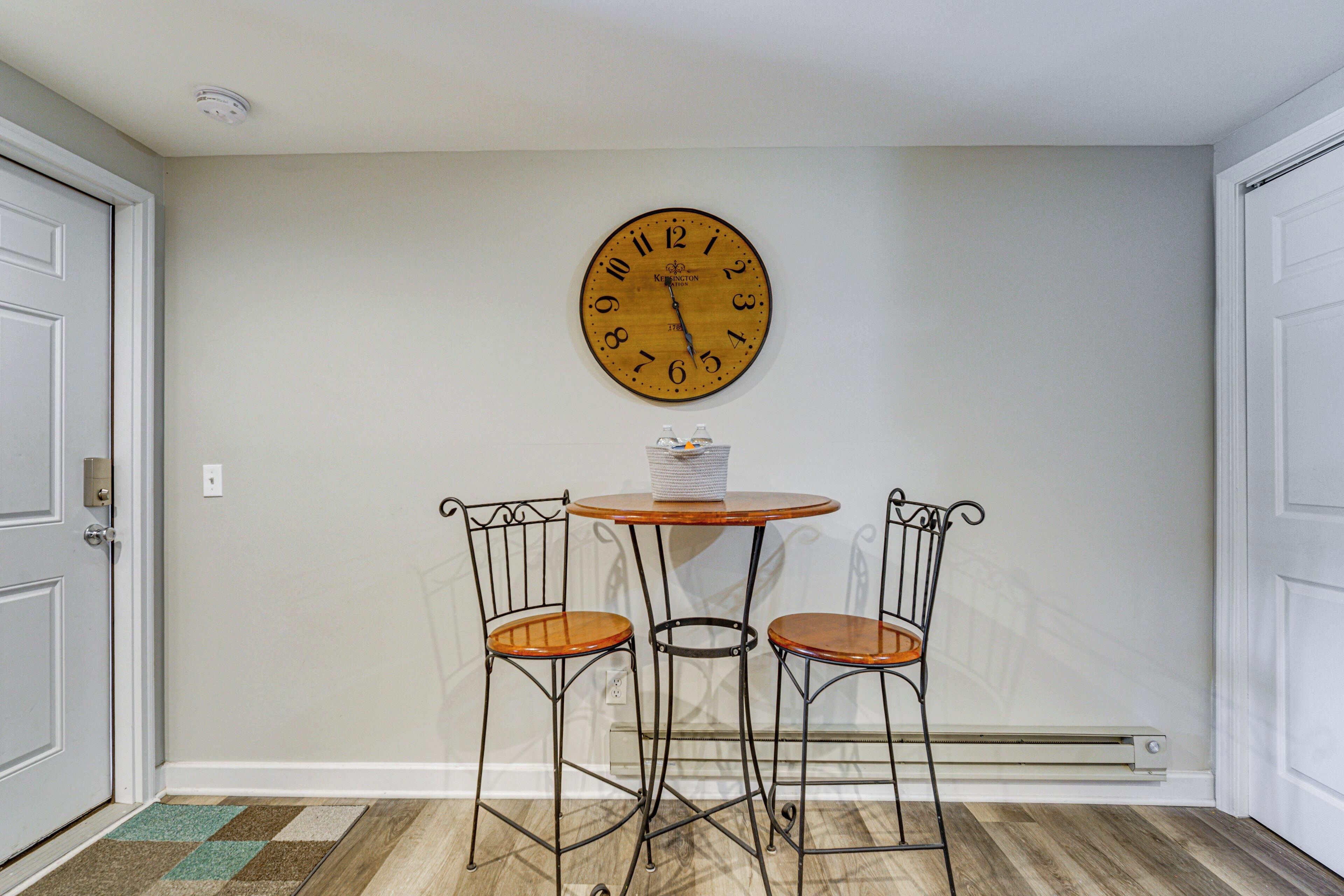 A room with a wooden clock, two metal chairs, a small round table, and a door.