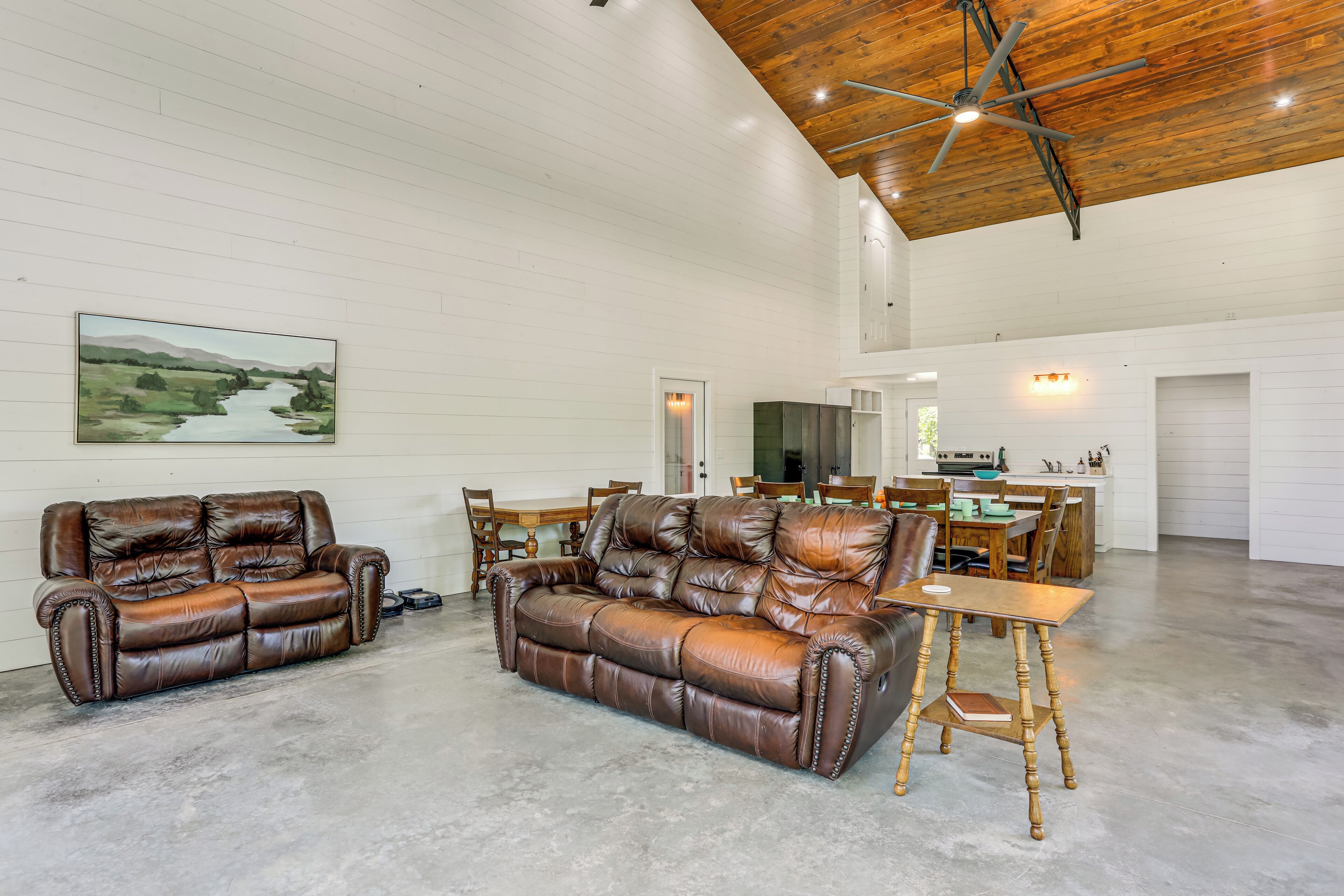 A spacious living area with two leather sofas, a dining table, and a kitchen in the background.