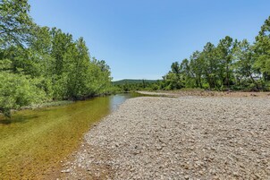 Um rio de águas cristalinas, cercado por árvores e um caminho de cascalho.