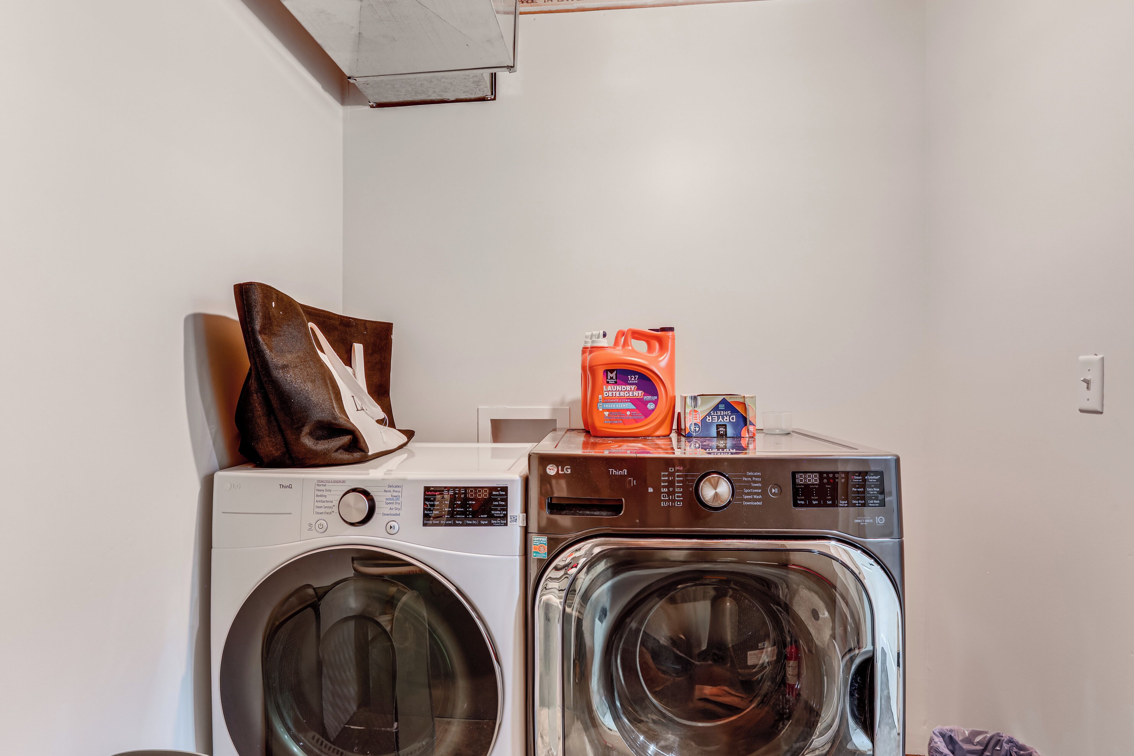 A laundry area with two washing machines, a brown bag, and a detergent bottle.