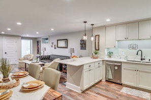 A modern kitchen with white cabinetry, a central island, pendant lighting, and a dining area with a table set for four. - Explore Historic Dtwn Staunton! Walkable Apartment (Staunton)