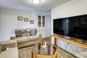 Un salón con un sofá color crema, una mesa de centro de vidrio, un televisor y fotografías enmarcadas en la pared.