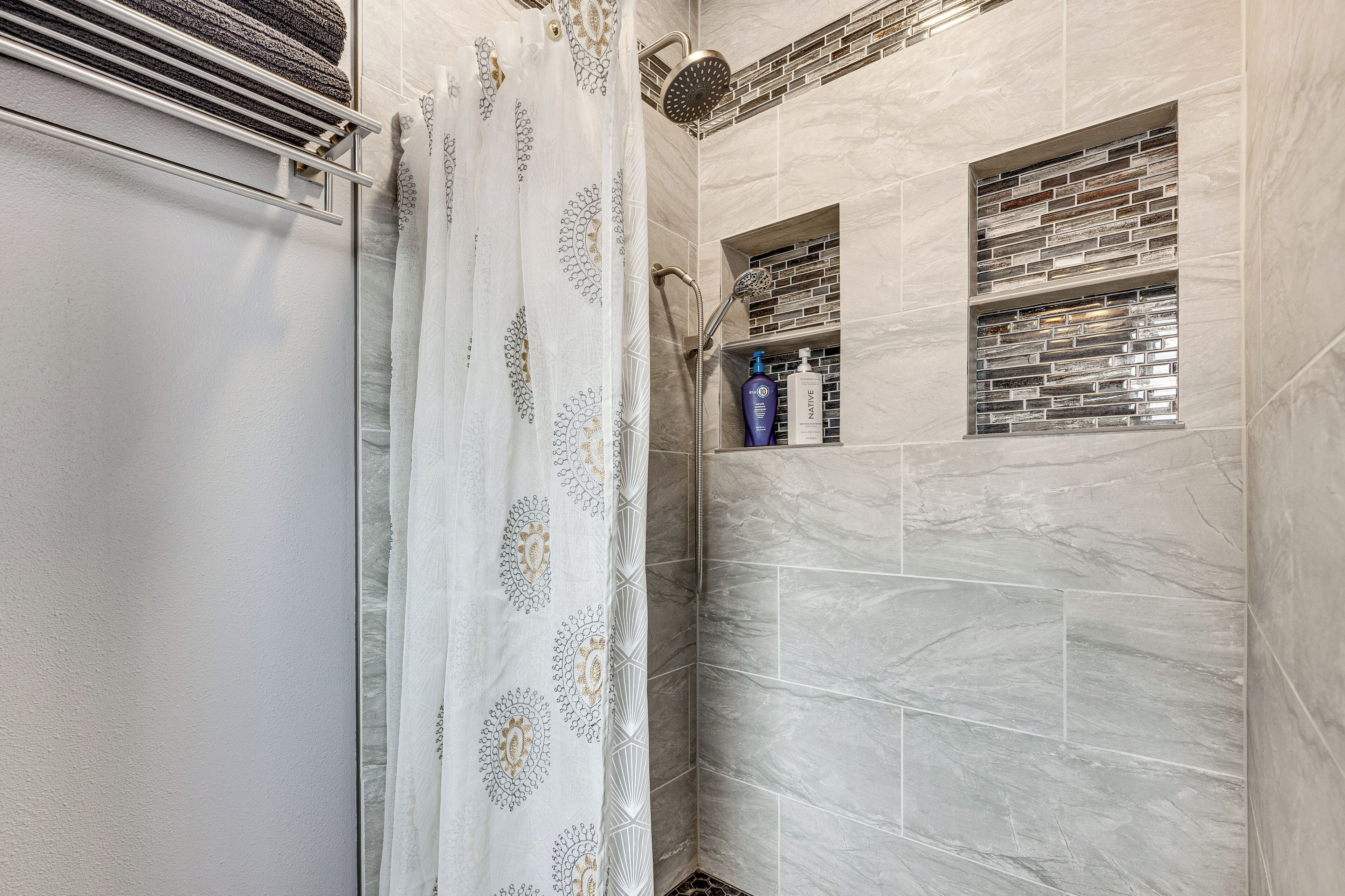 A bathroom with a shower, a towel rack, and a shelf with toiletries.