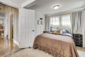 Un dormitorio con una cama grande, una puerta, una ventana con cortinas y un aparador.