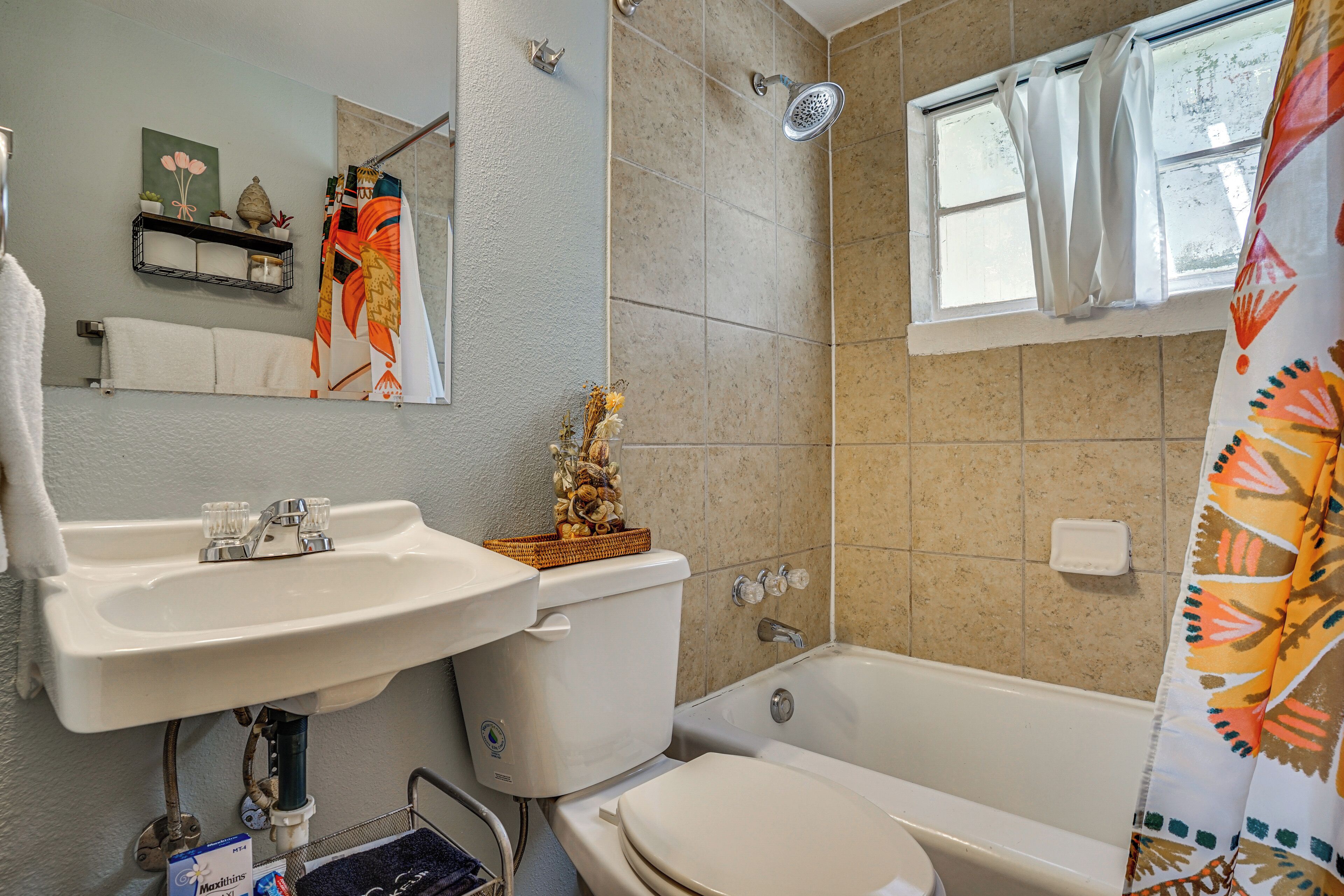 A bathroom with a sink, toilet, bathtub, shower, and a window with curtains.