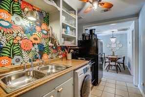 A kitchen with a colorful floral backsplash, a double sink, a black refrigerator, and a dining area with a chandelier. - 5 Mi to Will Rogers Center! Private Oasis w/ Grill (Fort Worth)