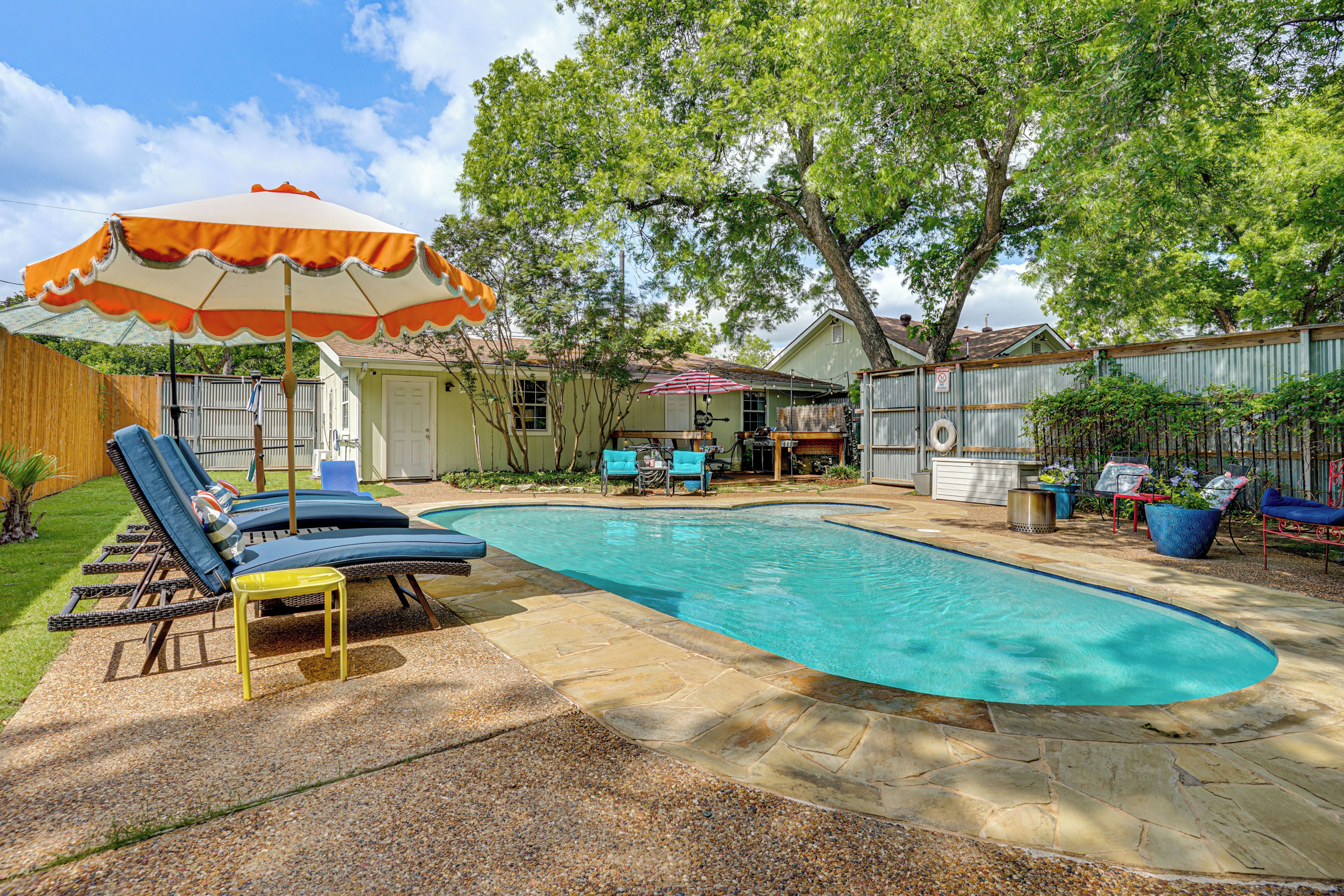 A backyard with a swimming pool, lounge chairs, and a covered umbrella.