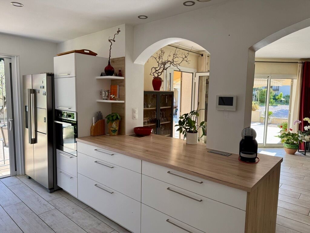 Uma cozinha moderna com frigorífico embutido, armários brancos, bancada de madeira e vista para o exterior através de um arco.