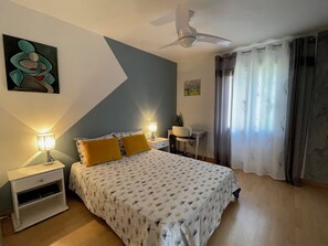 Ein Schlafzimmer mit Bett, Nachttischen, einem Schreibtisch, einem Deckenventilator und einem Fenster mit Vorhängen.