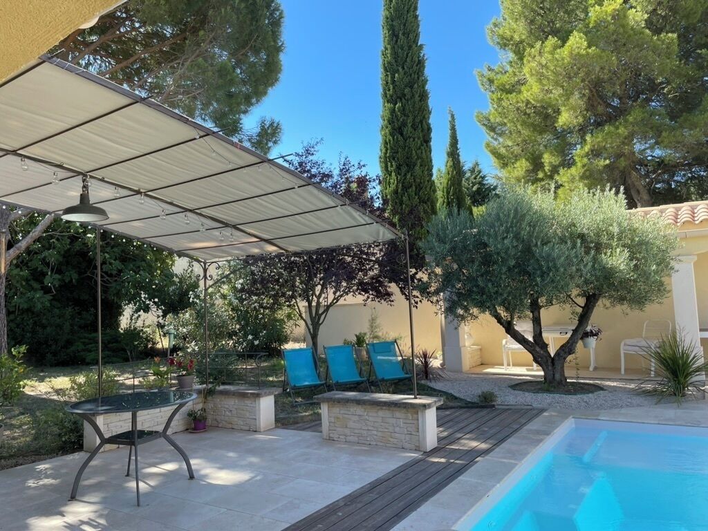 Zona de piscina amb una pèrgola, gandules i una taula petita.